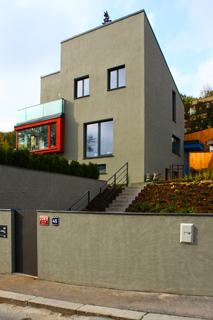 Fasáda celého domu je z betonové stěrky STO - beton optik, barevné prvky fasády (červený arkýř a modrý vstup) jsou natřené v příslušné barvě na tenkovrstvou zateplovací omítku STO